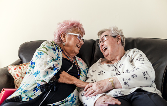 Older ladies laughing on sofa - stock