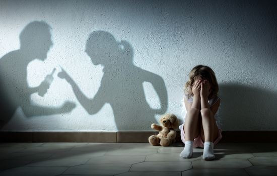 A picture of a little girl that is scared holding her head in her hands. There is a shadow of man holding what appears to be a bottle of alcahol clenching his fist arguing with a woman