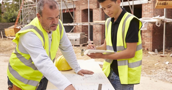 Older builder showing apprentice how to measure