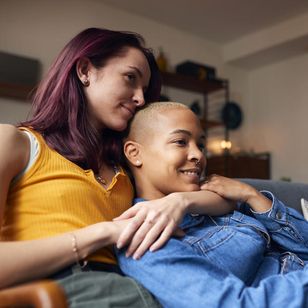 Female Couple Lying On Sofa At Home Watching TV And Relaxing Together