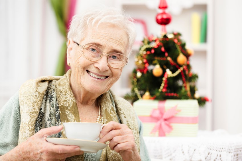 Old lady drinking tea in front of a Christmas tree