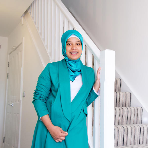 Women wearing a hijab standing at the foot of her stairs smiling