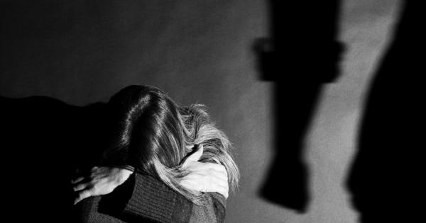 A black and white image of a lady sat on the floor with her head in her hands, and a shadow of an arm in a clenched fist insinuating a situation of domestic violence