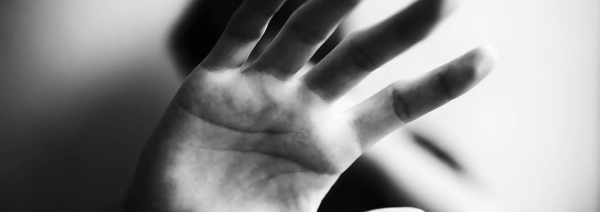 A black and white photo of a hand being held up to the camera gesturing to stop