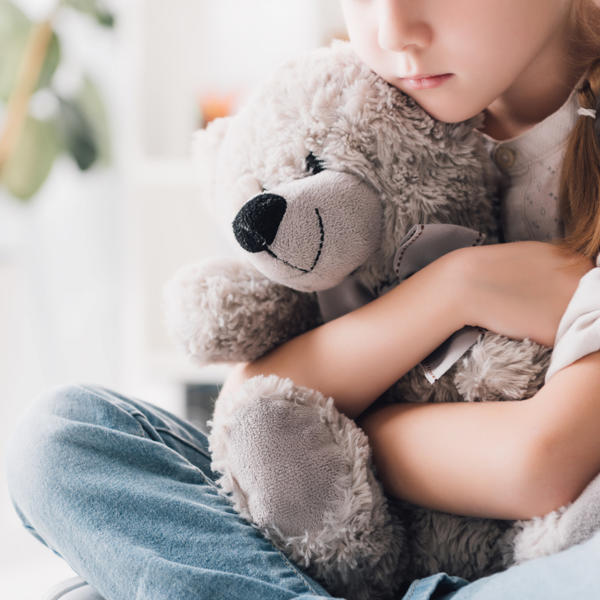 Cropped shot of depressed little child embracing her teddy bear